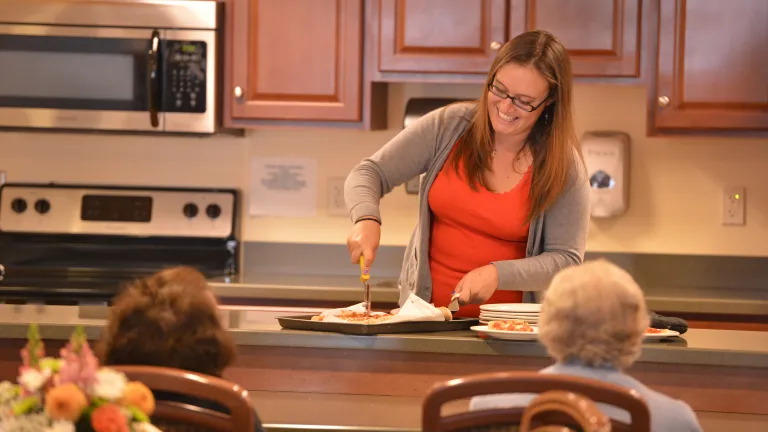 An employee prepares a meal in front of awaiting memory care residents