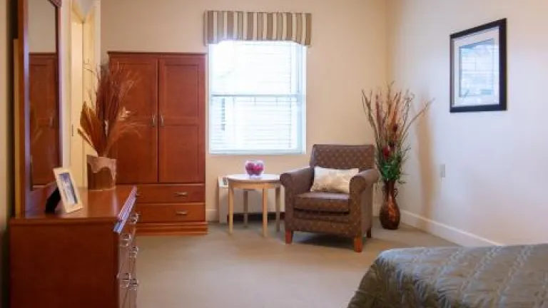 A bedroom with a dresser, armoire, armchair, and bed