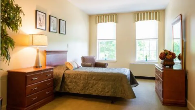 A cream-colored bedroom with dark wood furniture and a dark green bedspread