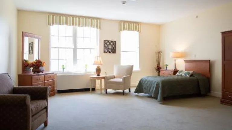 A spacious bedroom with large windows, two armchairs, a twin bed