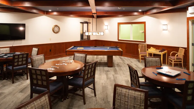 The game room at Kingsway Village with a pool table and several four-person tables with board games