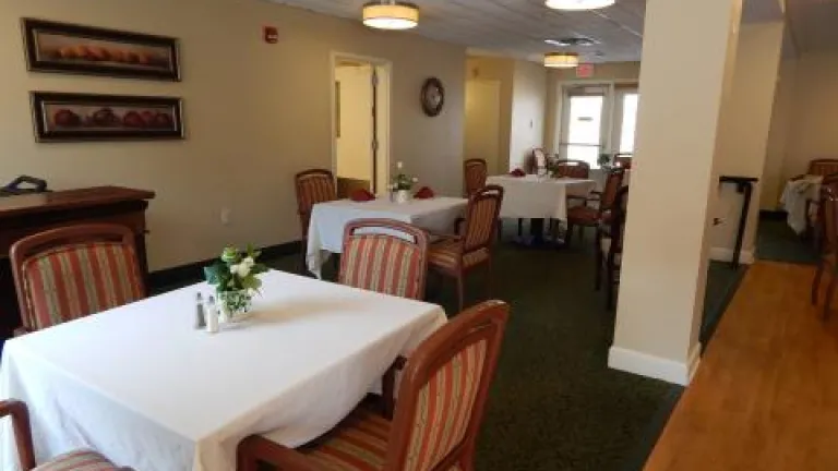 A dining room with red striped chairs at square tables with table cloths