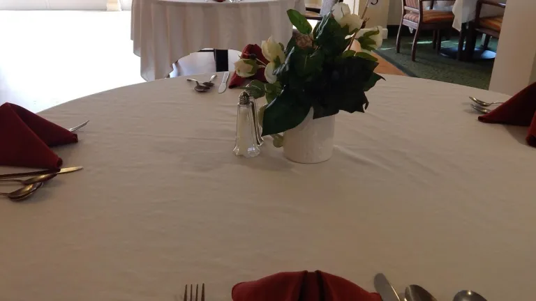A dining table with a white table cloth and four place settings with red napkins