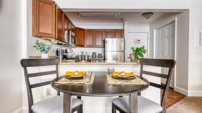 A two-person dining table with yellow place settings in front of a kitchen with dark cabinets