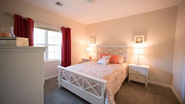 A bedroom with warm lighting, red drapes, and a bed with pink throw pillows and patterned comforter