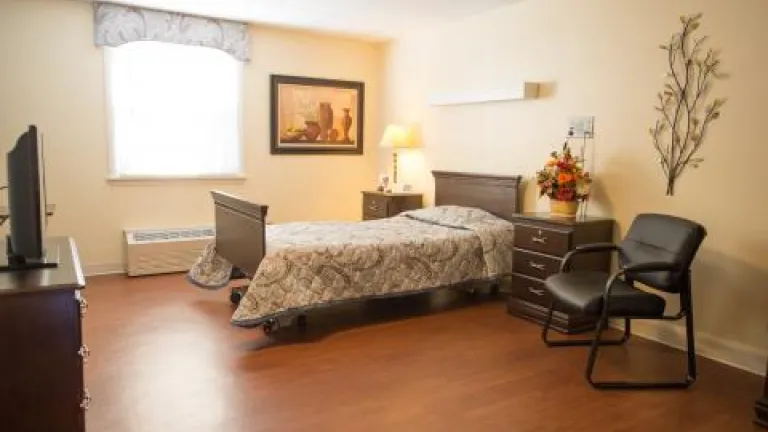 A spacious private room with a twin bed, bedside tables, guest chair, and bright window