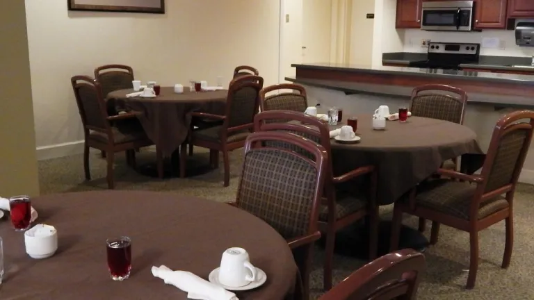 Memory care dining room, three round brown tables can be seen with coffee mugs and place settings. 