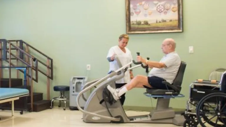A nurse assisting a man in a recumbent exercise machine