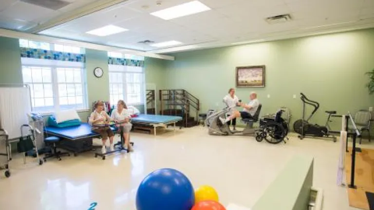 Two residents with nurses performing physical therapy activities in a large green room