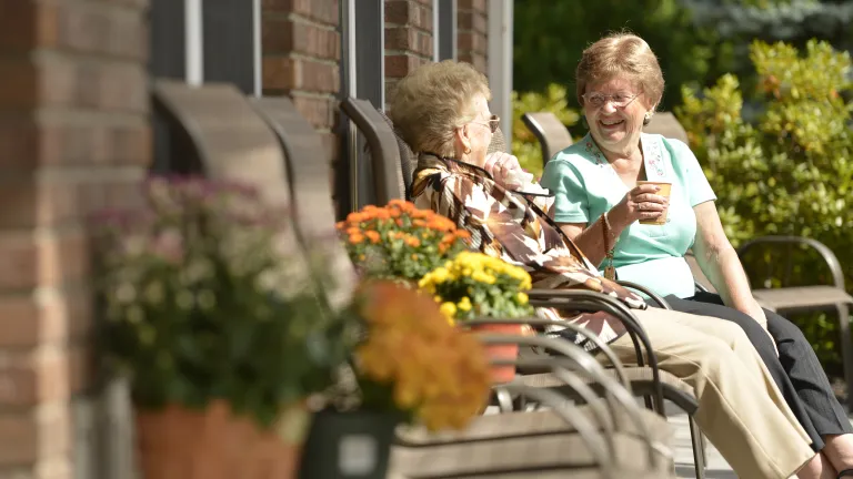 Assisted living residents sit on the patio in the sunshine chatting