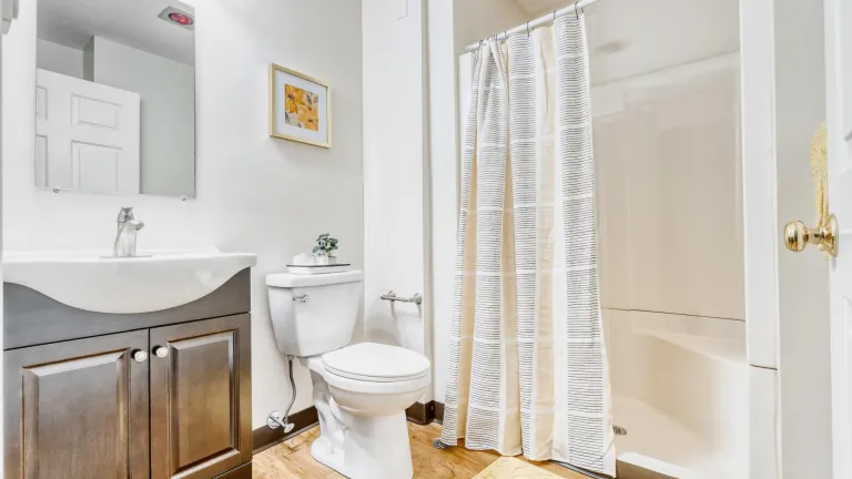 A white bathroom with dark wood vanity, light wood floors, and walk-in shower