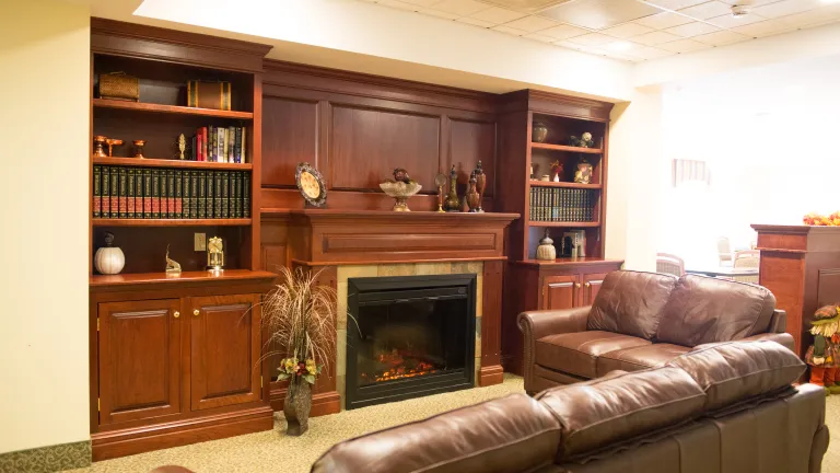 A grand fireplace with built in shelves surrounding it can be seen in a room with two large brown leather couches at the Memory Care Center