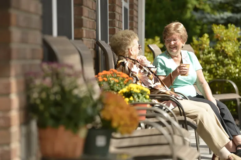 Assisted living residents sit on the patio in the sunshine chatting