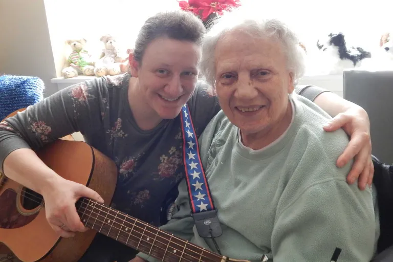 An elderly resident posing for a photo with a musician holding a guitar
