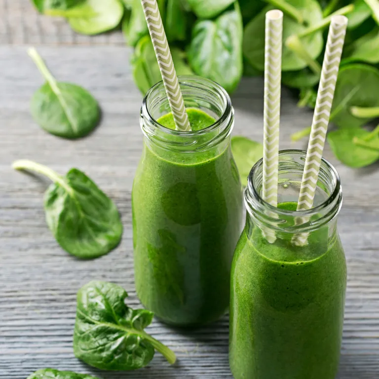 Two green smoothies in glass bottles with paper straws