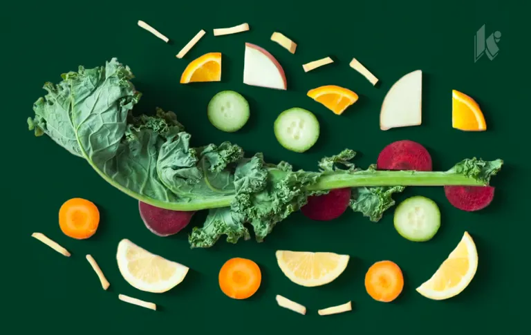 A photo of various healthy fruits an vegetables silhouetted over a dark green background. Veggies include kale, cucumber, radish, carrots. Fruits include orange slices and apples. 