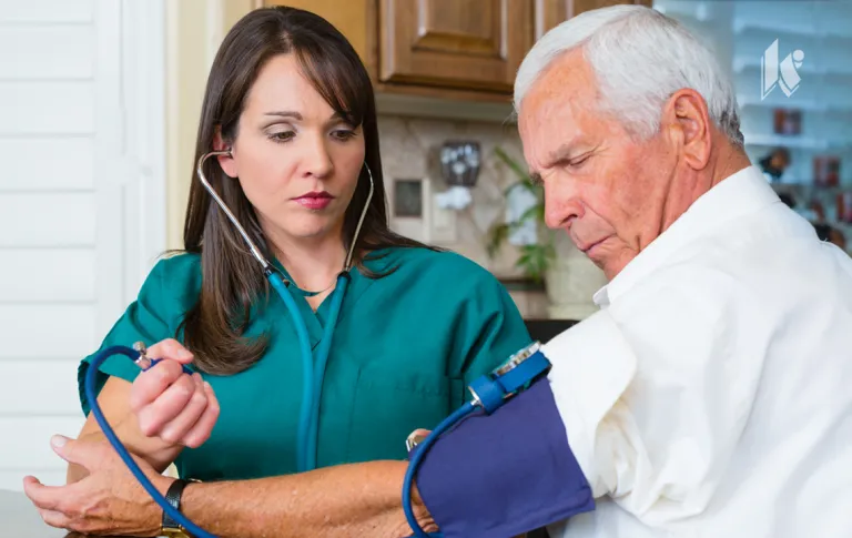 A nurse is visiting a senior living resident in their apartment and taking their blood pressure with a cuff. 