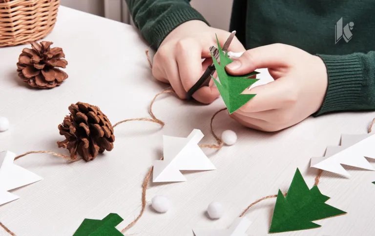 DIY Christmas home decor from natural materials. Hands make garland of paper trees, twine and cones.