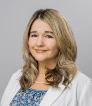 Farra Foster headshot, she has medium length blonde hair and is wearing a white blazer, blue floral blouse, and has a pearl necklace on. 