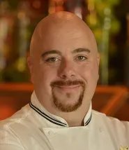 Chef Paul headshot. Paul is wearing his white chefs jacket, he is bald and has a goatee. 