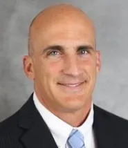 James Farnan wears a simple suit and stands in front of a grey photo background 