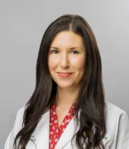 Headshot of a woman with long brown hair, wearing a white doctors coat and a red blouse underneath